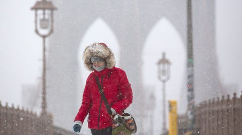 Una mujer camina bajo la nieve por el puente de Brooklyn.