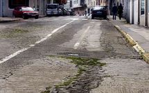 El empedrado de la calle est� destrozado y los coches tienen que sortear baches y adoquines. 