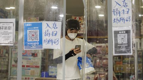 Un repartidor sale de una tienda de Shanghi que tiene la entrada cubierta de plsticos por el covid