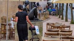 Una mujer desinfecta un asiento de una terraza del centro de Oviedo