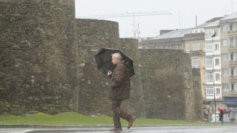 Un hombre camina bajo la lluvia junto a la muralla de Lugo.