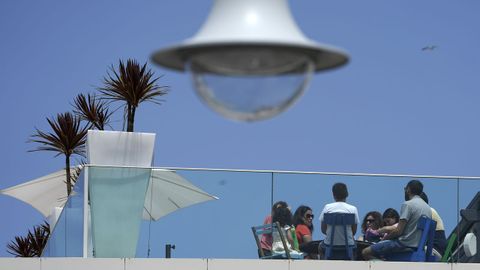 Turistas disfrutan del tiempo en una terraza en una soleada mañana en Gijón