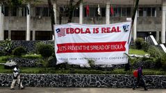 Fotograf�a de archivo fechada el pasado 31 de julio del 2014 que muestra a varios liberianos caminando frente a un cartel que alerta sobre los peligros del �bola en el Ayuntamiento de Monrovia (Liberia)