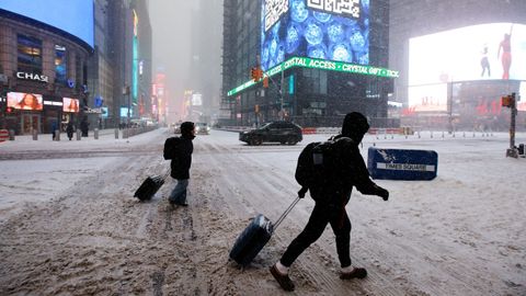 Dos personas arrastran sus maletas sobre la nieve por Times Square