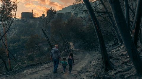 Un hombre mayor y dos nios caminan cerca de Santo Estevo (Pantn) y en medio del paisaje quemado por el incendio que afect a los caones del Sil y el Cabe, con la iglesia del poblado de A Chaira al fondo