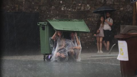 Dos personas en Santiago refugiadas esta tarde bajo la tapa de un contenedor al sorprenderlas una intensa lluvia