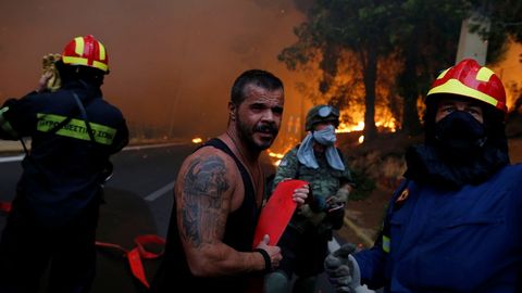 Bomberos, soldados y residentes locales llevan una manguera durante un incendio forestal arde en la ciudad de Rafina, cerca de Atenas