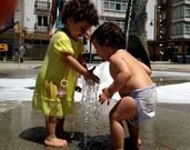 Dos ni�os juegan con el agua en una fuente de Cee.