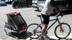 Imagen de archivo de un ciclista con con remolque para transportar nios