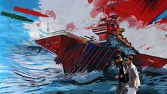 Dos personas caminan en Teher�n ante un mural que muestra un ataque a un buque de guerra de Estados Unidos.