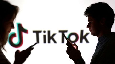 Dos j�venes posan con sus m�viles frente a un cartel de la red social TitTok.