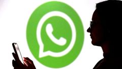 Una persona mirando el m�vil con el logo de WhatsApp al fondo