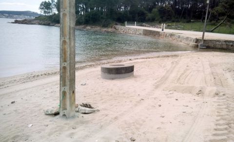 En medio del arenal hay un poste y una alcantarilla. 