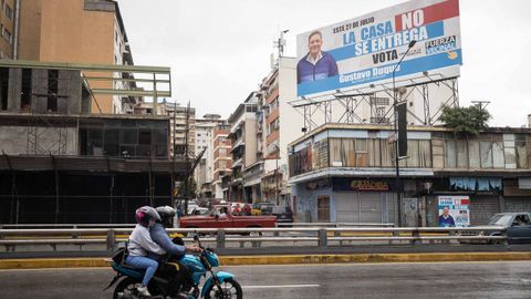 Personas en motocicleta pasan frente a un valla del alcalde del municipio Chacao de Caracas, Gustavo Duque, este sábado en Caracas (Venezuela).