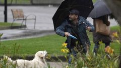 Un hombre se dispone a lanzar un frisbee a su perro esta mañana bajo la lluvia en Oviedo.