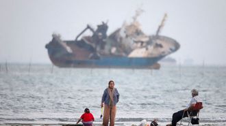 Personas en una playa del estrecho de Ormuz ante un petrolero