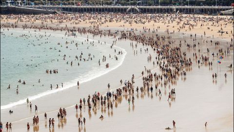 Donostiarras y visitantes pasean al mediodía por la playa de La Concha de San Sebastián, dónde esta tarde ya comenzaron a notarse chubascos tormentosos