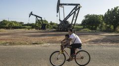 Una mujer conduce junto a un ni�o en una bicicleta frente a unas estructuras petroleras en Cabimas (Venezuela).