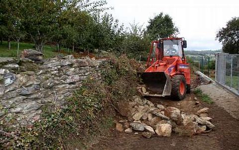La pala de la Diputaci�n lleva a cabo el derribo de un muro para ampliar la pista en Sestelo-Vilar.