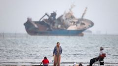 Personas en una playa del estrecho de Ormuz ante un petrolero