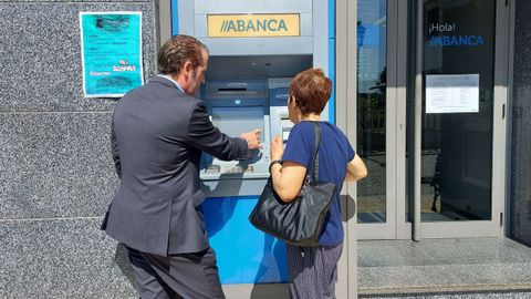 Un empleado de banca enseando a una persona mayor a operar con un cajero (imagen de archivo)