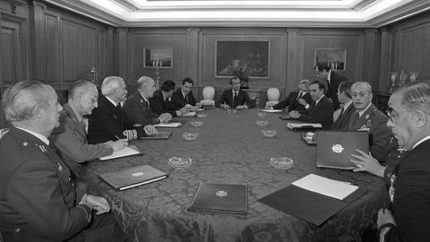 Juan Carlos I, presidiendo la Comisi&oacute;n de Defensa. Celebrada el 24 de febrero de 1981 en Madrid, participan el presidente en funciones Adolfo Su&aacute;rez; el vicepresidente Manuel Guti&eacute;rrez Mellado; el ministro del Interior, el gallego Juan Jos&eacute; Ros&oacute;n; el director de Seguridad del Estado, Francisco Laina; y el teniente general Jos&eacute; Gabeiras Montero, entre otros altos cargos civiles y militares.