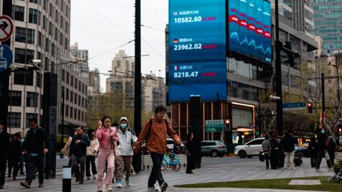Varias personas caminan por una calle de Shanghai bajo una gran pantalla que muestra los �ltimos datos burs�tiles.