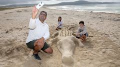 Suso Paz y sus dos hijos posan en la playa de A Ladeira junto a un cocodrilo de arena que acaban de crear