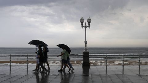 Varias personas se protegen con el paraguas de la lluvia, en el paseo de muro de la playa de San Lorenzo de Gij�n
