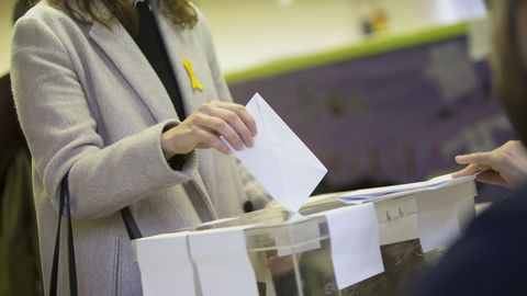 Una mujer con un lazo amarillo deposita su voto en un colegio electoral de Barcelona