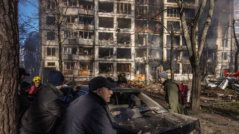 Unas personas intentan mover un coche daado frente a un edificio residencial en llamas que fue alcanzado por un bombardeo de artillera, en Kiev, Ucrania