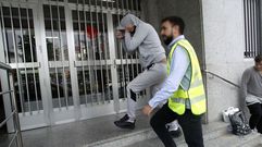 Uno de los cuatro detenidos se tapa la cara al entrar esposado en el juzgado de Chantada, custodiado por un guardia civil de paisano