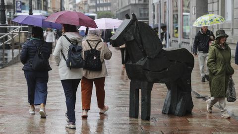 Un grupo de mujeres con paraguas junto a la escultura de Manolo Vald�s Asturc�n, en la plaza de la Escandalera de Oviedo, 