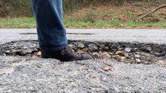 Un vecino introduce un pie en uno de los baches de la carretera de A Barrela a Os Peares para que se vea su profundidad