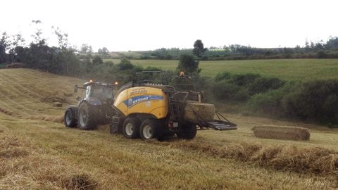 Un tractor empacando hierba seca en una finca del concello de Mazaricos