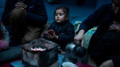Marjan Hosini, de 3 a�os, calienta sus manos al lado de sus padres, en un refugio temporal aleda�o al campamento de Moria
