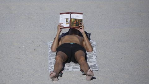 Un hombre lee un libro en la playa.