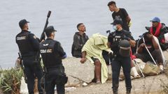 Varios migrantes conversan en la playa del Trampol�n bajo la presencia de tres agentes de la Polic�a Nacional.