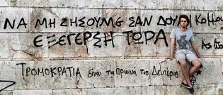 Un seguidor de Syriza se sienta al lado de un grafiti que dice �Revoluci�n ahora, no vivas como un esclavo, revoluci�n ya�.