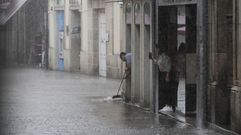 Un empleado de una tienda del centro de Monforte tratar de desviar con una escoba el agua que corre por la calle en un momento de lluvia intensa este martes por la tarde 