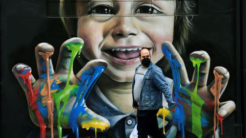 Un hombre pasea junto a un grafiti del artista callejero Bastian Prendes en una calle de Pola de Siero