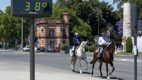 Dos jinetes pasan por delante de un termómetro en Sevilla