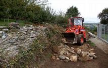 La pala de la Diputaci�n lleva a cabo el derribo de un muro para ampliar la pista en Sestelo-Vilar.