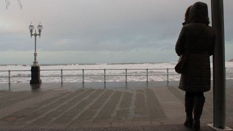 Una mujer observa un temporal en el paseo del Muro de Gijn