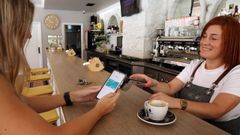 Una clienta paga la consumici�n con el tel�fono m�vil en la cafeter�a Arcos, en Ribeira