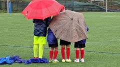 Ni�os protegi�ndose de la lluvia bajo paraguas debido a la falta de banquillo en un partido de f�tbol en O Carballi�o