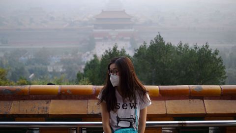 Una mujer con mascarilla posa para una foto con la Ciudad Prohibida entre una niebla de contaminacin.