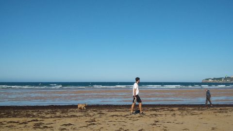 Basura arrastrada por la marea a la playa de San Lorenzo de Gij�n.Un usuario de la playa, tras recoger una de las botellas de pl�stico