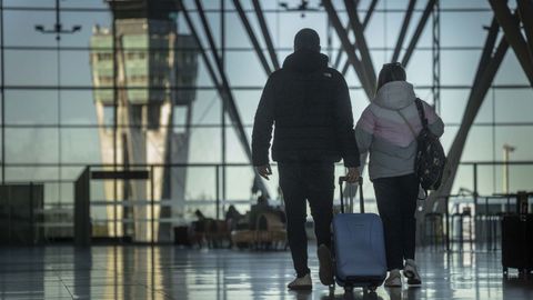 Dos pasajeros caminan con sus maletas por la terminal del aeropuerto de Santiago-Rosala de Castro.