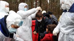Sanitarios bielorrusos ayudan a un grupo de migrantes a prepararse para ser trasladados a un centro de acogida.